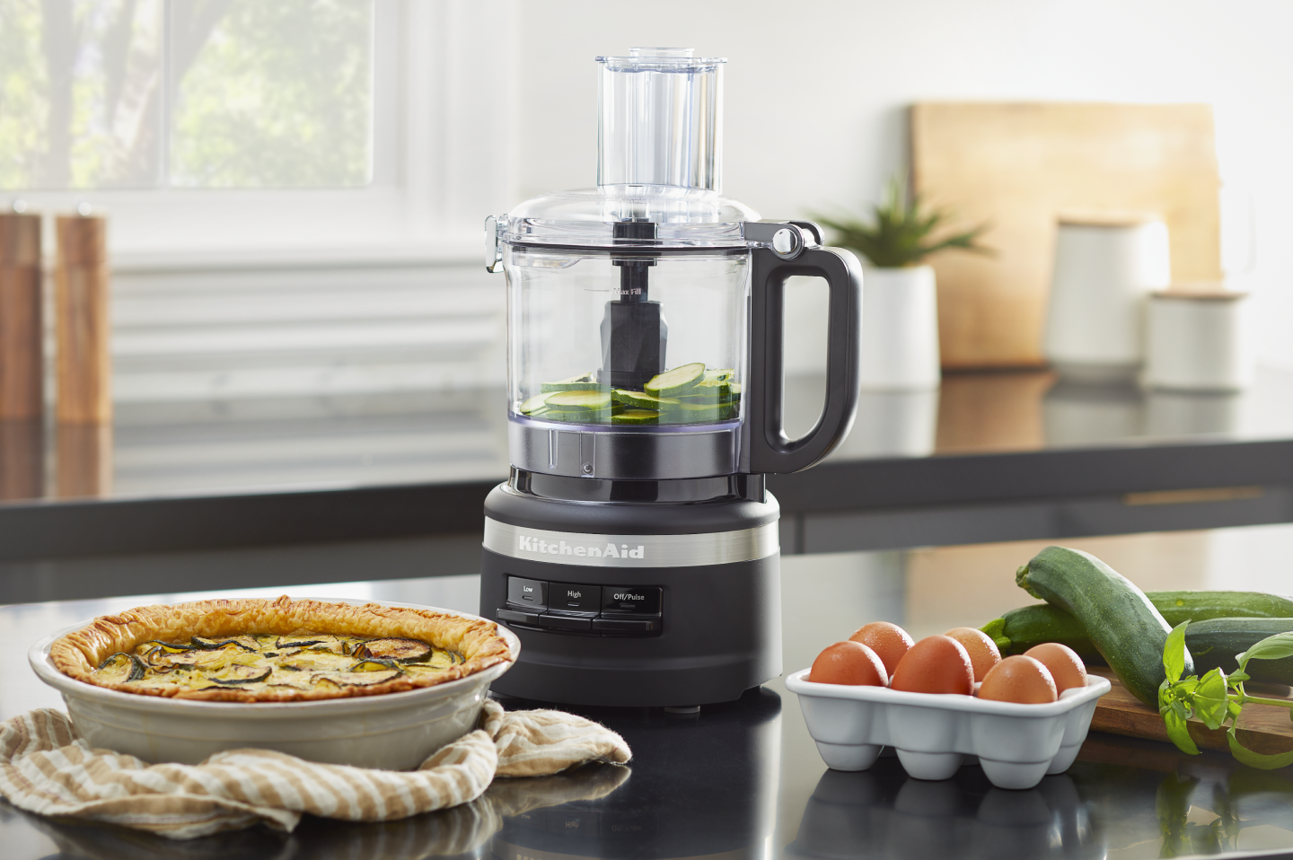 Sliced cucumbers in a black KitchenAid® food processor next to a vegetable quiche Sliced cucumbers in a black KitchenAid® food processor next to a vegetable quiche