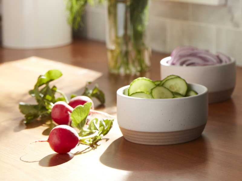 Sliced cucumbers inside a white bowl next to radishes
