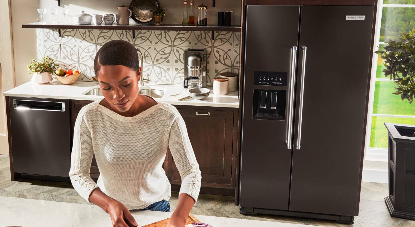 Person standing in front of a gray KitchenAid® side-by-side refrigerator with an exterior water and ice dispenser
