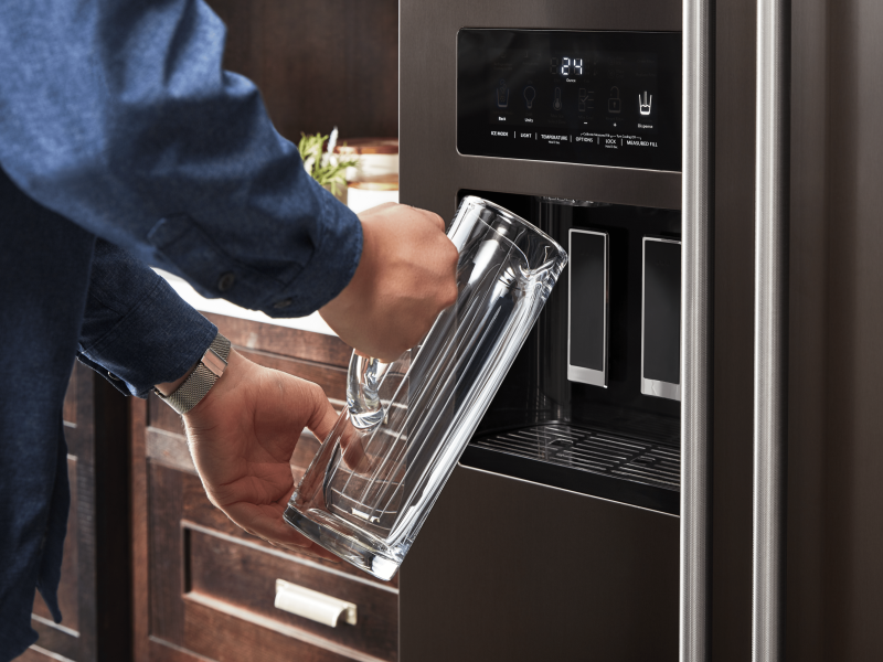 Person filling a pitcher at the refrigerator water dispenser Person filling a pitcher at the refrigerator water dispenser