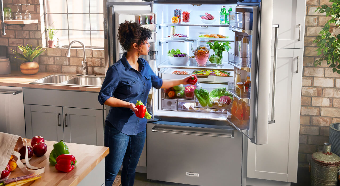 A person placing red and green peppers in a crisper drawer A person placing red and green peppers in a crisper drawer