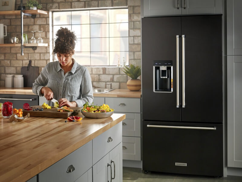Person preparing food at a kitchen island in front of a black KitchenAid® refrigerator