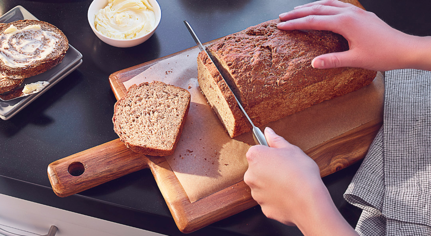 Person slicing a loaf of bread on a wooden cutting board Person slicing a loaf of bread on a wooden cutting board