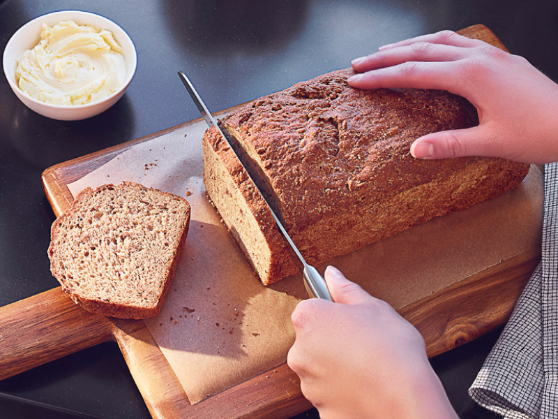 Person slicing a loaf of bread on a wooden cutting board Person slicing a loaf of bread on a wooden cutting board