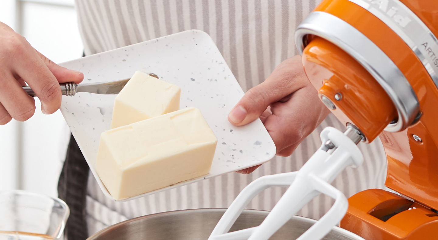 Person adding butter to a KitchenAid® stand mixer bowl Person adding butter to a KitchenAid® stand mixer bowl