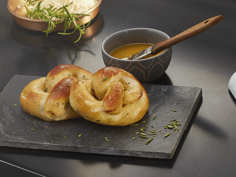 Soft pretzels on a cutting board next to a dish with melted butter and basting brush
