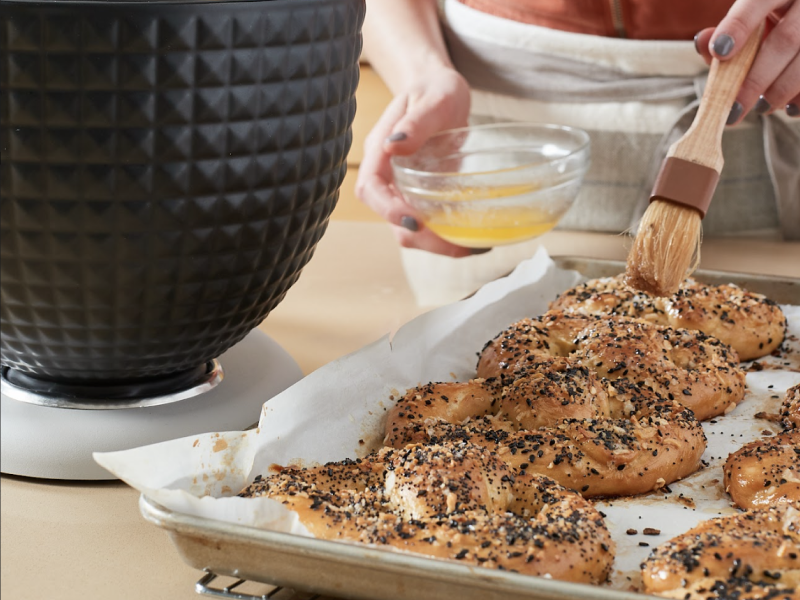 Person applying an egg wash to a tray of everything pretzels