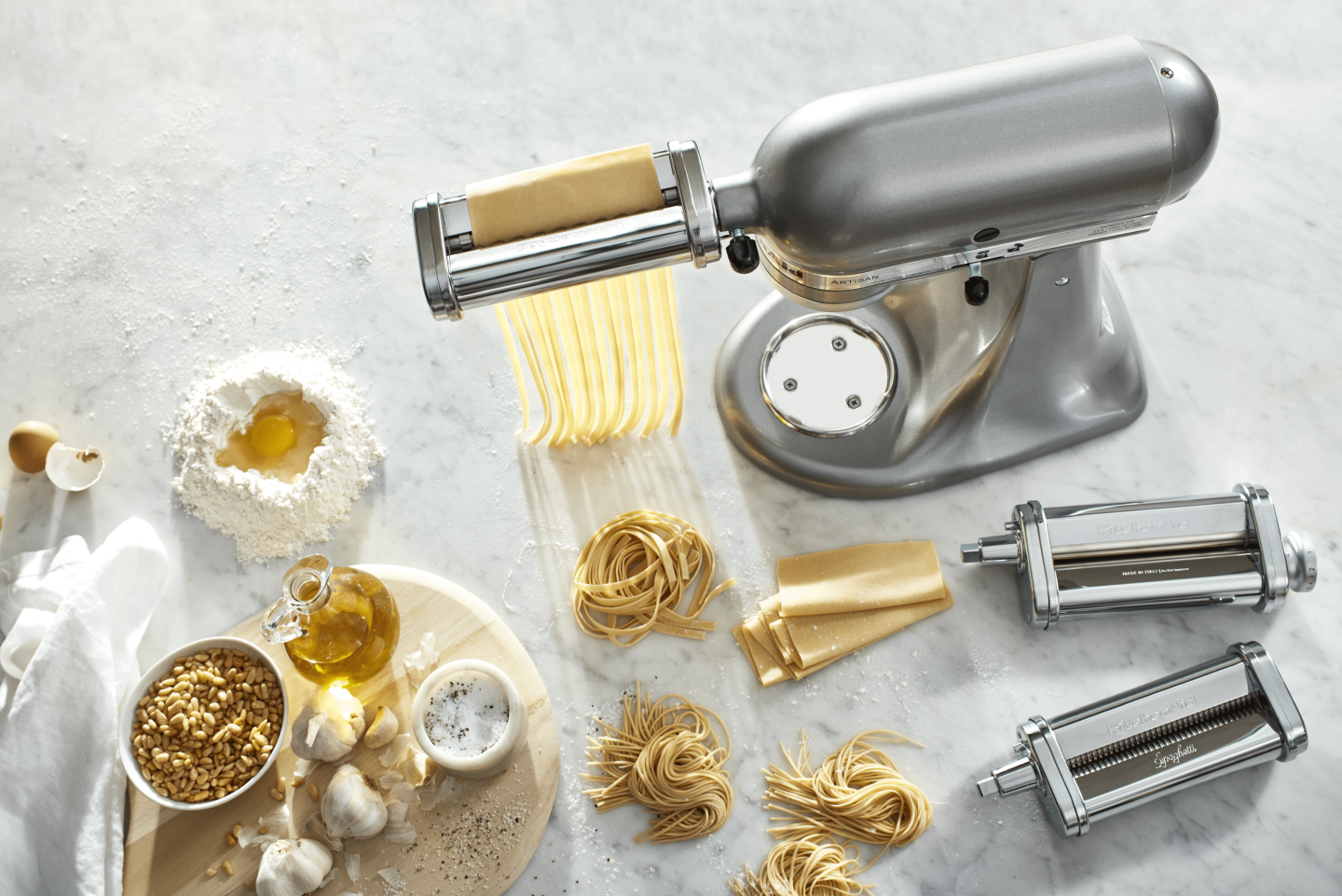 Silver KitchenAid® Stand Mixer with pasta-making attachments surrounded by mounds of fresh pasta and pasta ingredients  Silver KitchenAid® Stand Mixer with pasta-making attachments surrounded by mounds of fresh pasta and pasta ingredients