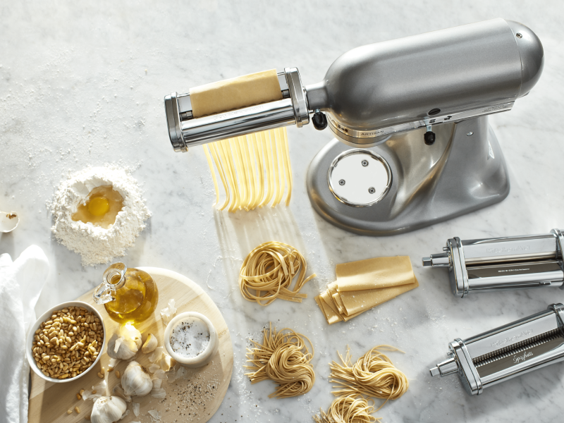 Silver KitchenAid® Stand Mixer with pasta-making attachments surrounded by mounds of fresh pasta and pasta ingredients  Silver KitchenAid® Stand Mixer with pasta-making attachments surrounded by mounds of fresh pasta and pasta ingredients