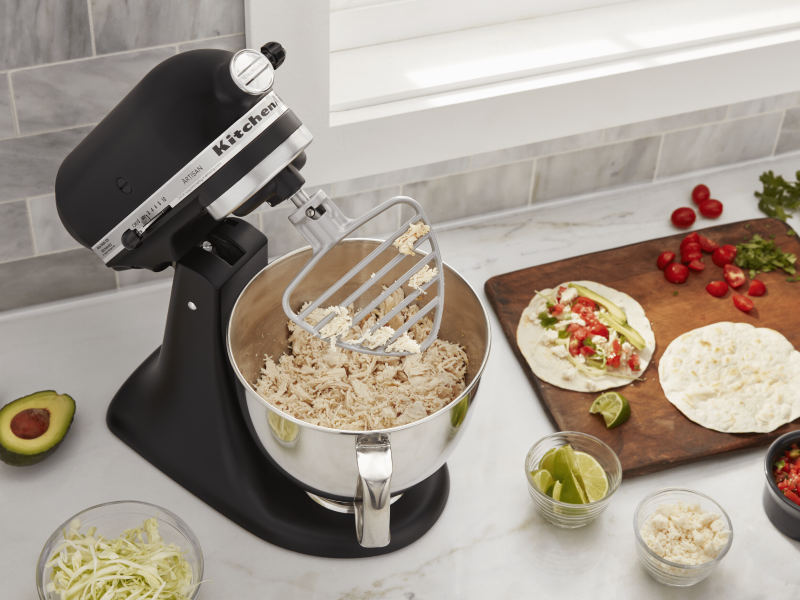 Black KitchenAid® Stand Mixer shredding chicken using the paddle attachment while surrounded by tortillas, salsa and taco fixings on a counter  Black KitchenAid® Stand Mixer shredding chicken using the paddle attachment while surrounded by tortillas, salsa and taco fixings on a counter