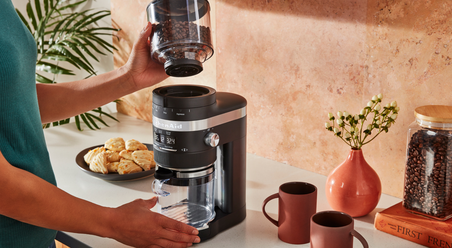 Person adding coffee beans to a coffee maker