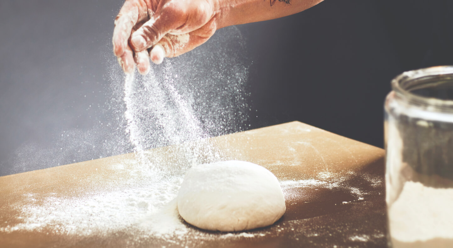 Person sprinkling flour over a ball of dough Person sprinkling flour over a ball of dough