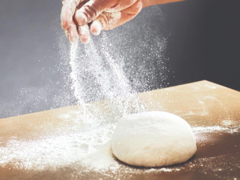 Person sprinkling flour over a ball of dough Person sprinkling flour over a ball of dough