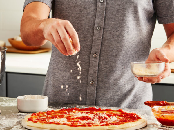 Person sprinkling cheese on a pizza