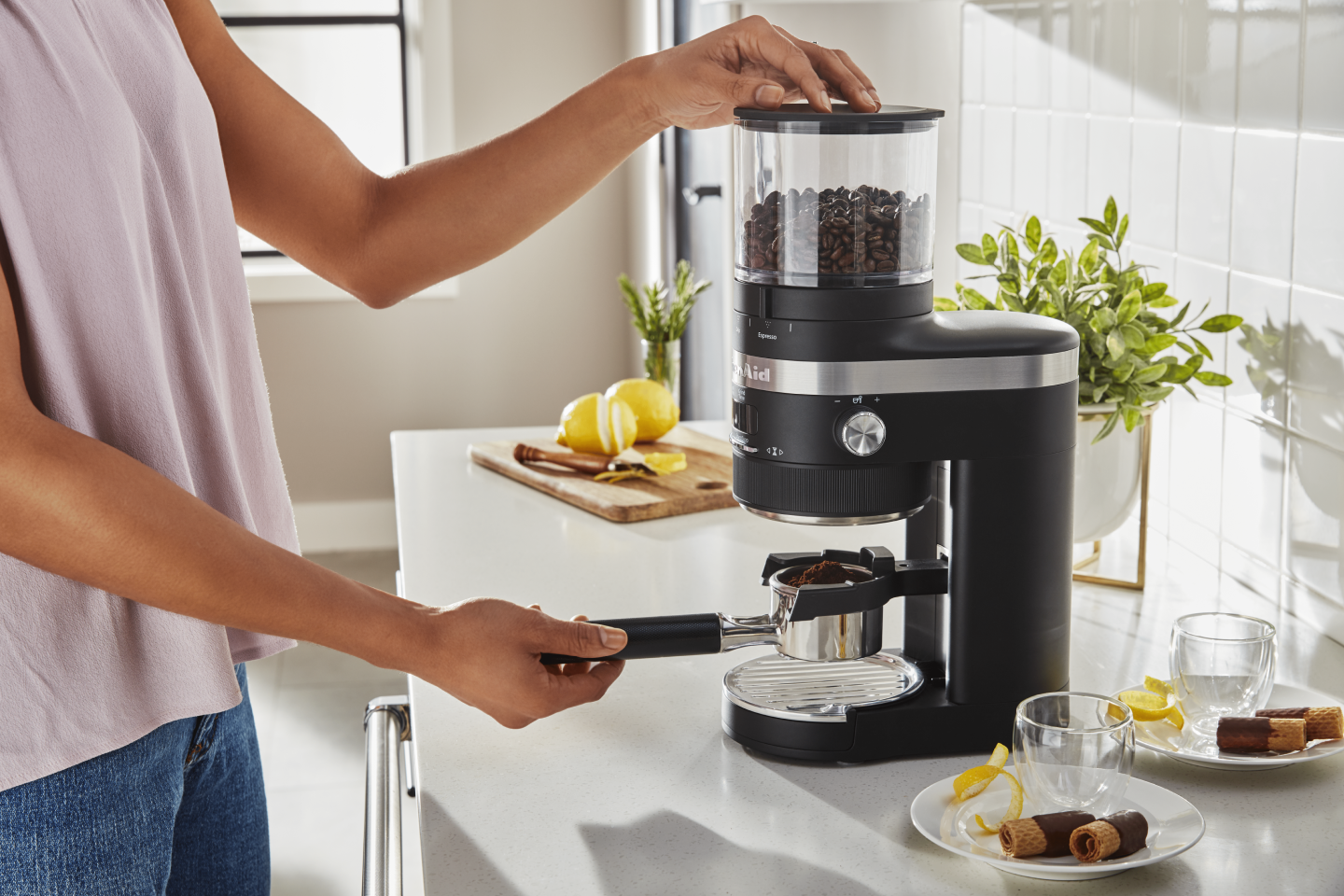 A woman using a black KitchenAid® Burr Coffee Grinder to process coffee beans A woman using a black KitchenAid® Burr Coffee Grinder to process coffee beans