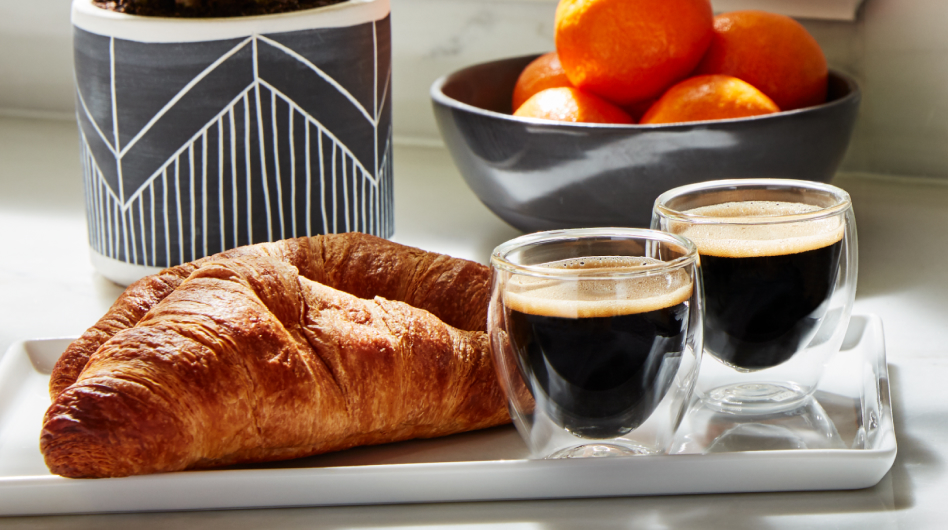 Croissants and cups of espresso on a tray in front of a bowl of oranges. Croissants and cups of espresso on a tray in front of a bowl of oranges.