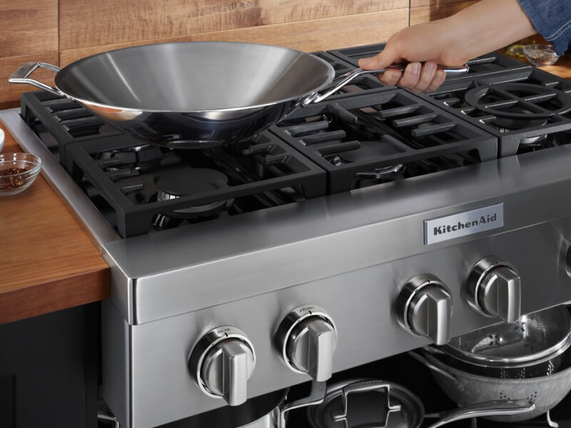A person placing a wok on a KitchenAid® gas commercial-style cooktop A person placing a wok on a KitchenAid® gas commercial-style cooktop