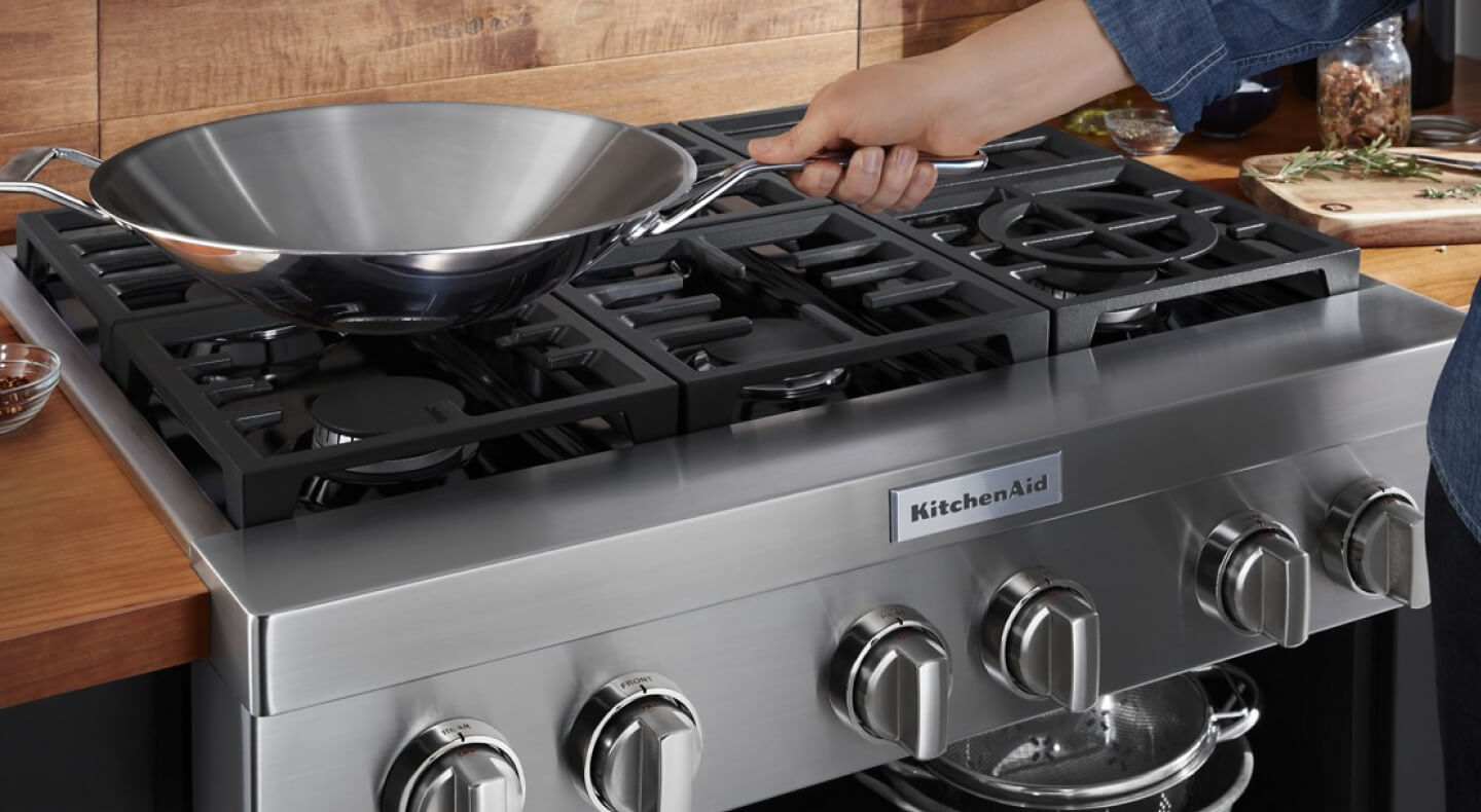 A person placing a wok on a KitchenAid® gas commercial-style cooktop A person placing a wok on a KitchenAid® gas commercial-style cooktop