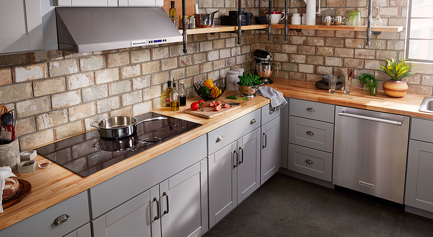 A kitchen with a glass cooktop and veggies on a cutting board nearby A kitchen with a glass cooktop and veggies on a cutting board nearby