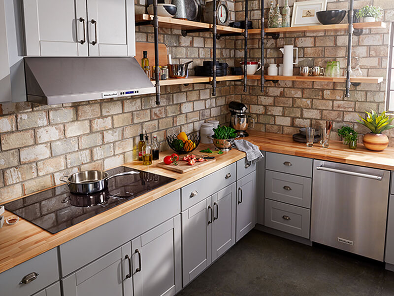 A kitchen with a glass cooktop and veggies on a cutting board nearby A kitchen with a glass cooktop and veggies on a cutting board nearby