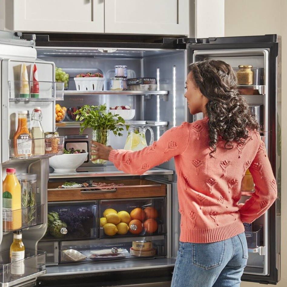Woman in pink sweater putting herbs in French door type of refrigerator Woman in pink sweater putting herbs in French door type of refrigerator