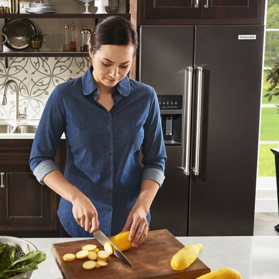 Woman preparing food in front of side-by-side fridge type in modern kitchen Woman preparing food in front of side-by-side fridge type in modern kitchen