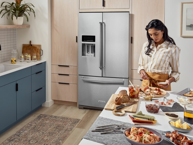 A woman preparing food at her kitchen island with a French door refrigerator in the background