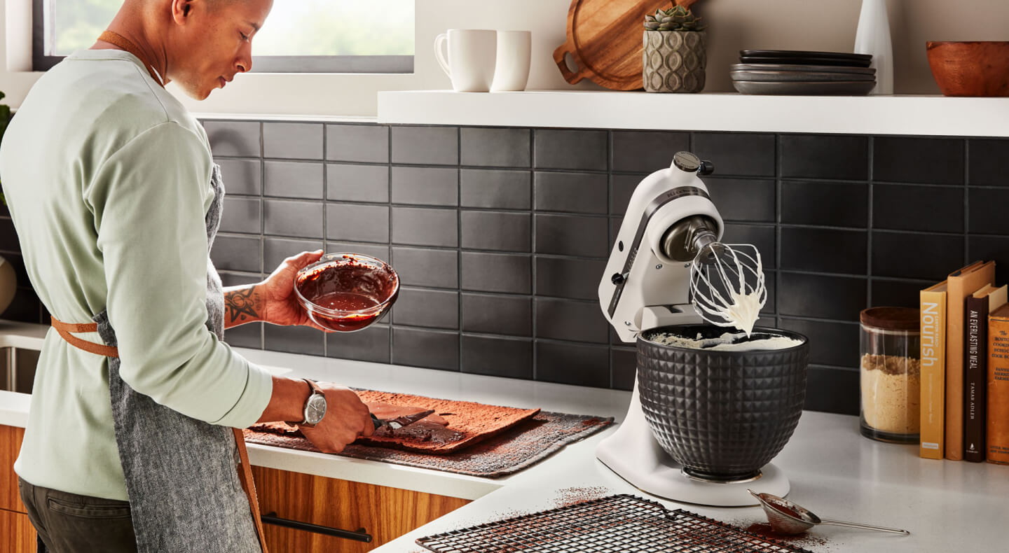A person with a bowl of melted chocolate standing next to a KitchenAid® stand mixer with a wire whisk accessory and whipped egg whites. A person with a bowl of melted chocolate standing next to a KitchenAid® stand mixer with a wire whisk accessory and whipped egg whites.