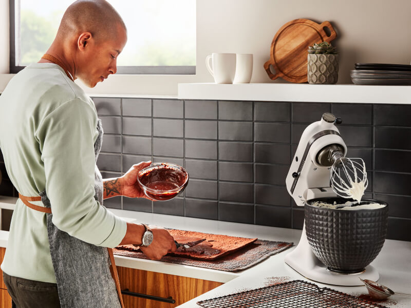 A person with a bowl of melted chocolate standing next to a KitchenAid® stand mixer with a wire whisk accessory and whipped egg whites. A person with a bowl of melted chocolate standing next to a KitchenAid® stand mixer with a wire whisk accessory and whipped egg whites.
