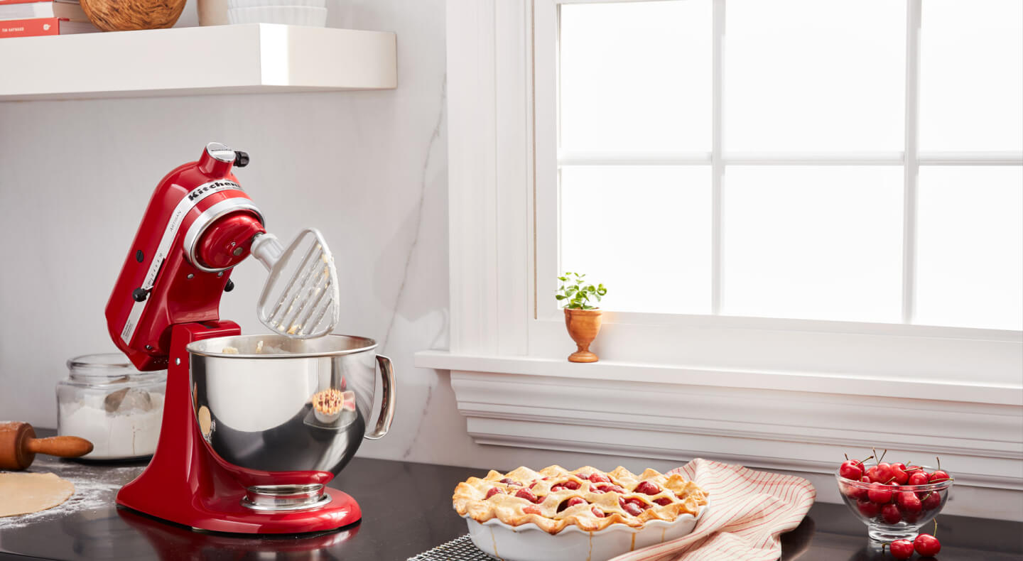 A KitchenAid® stand mixer with a pastry beater accessory next to a pie on the counter of a modern kitchen. A KitchenAid® stand mixer with a pastry beater accessory next to a pie on the counter of a modern kitchen.