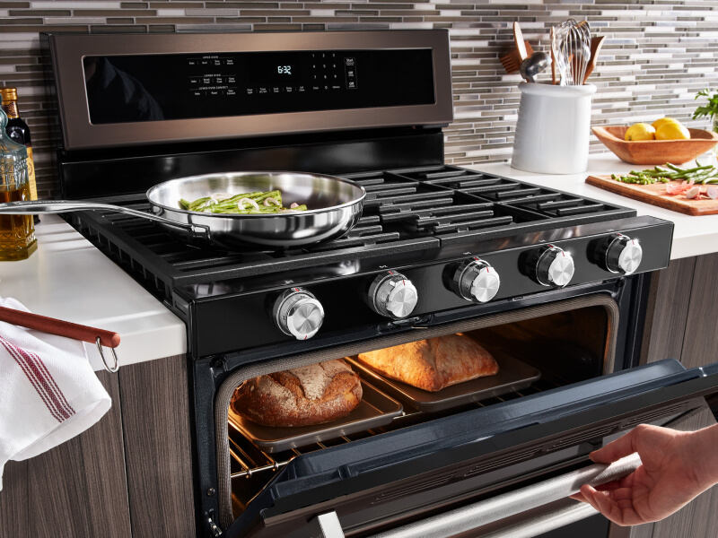 Vegetables cooking on a gas cooktop as bread bakes in the oven