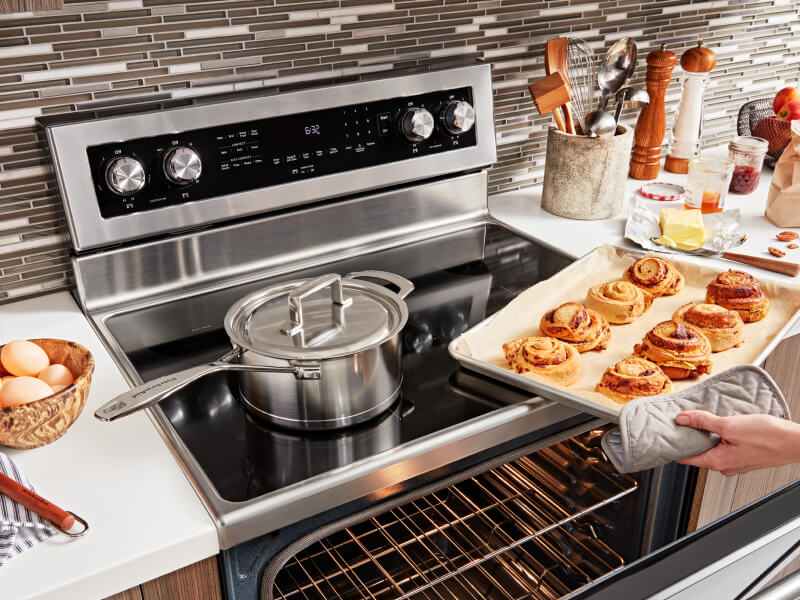 Person removing a tray of baked rolls from an electric range