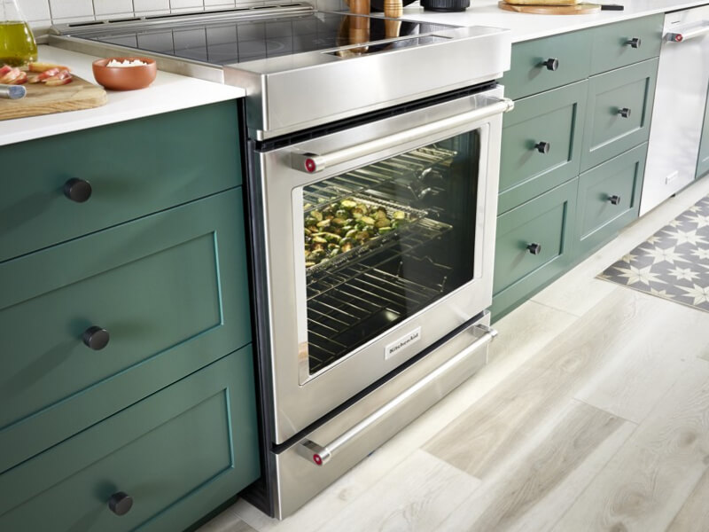 Stainless steel KitchenAid® induction range in a kitchen with green cabinets