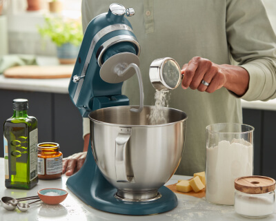 Person adding ingredients to a stand mixer bowl