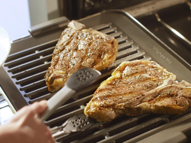 Person grilling meat on a grill oven attachment 