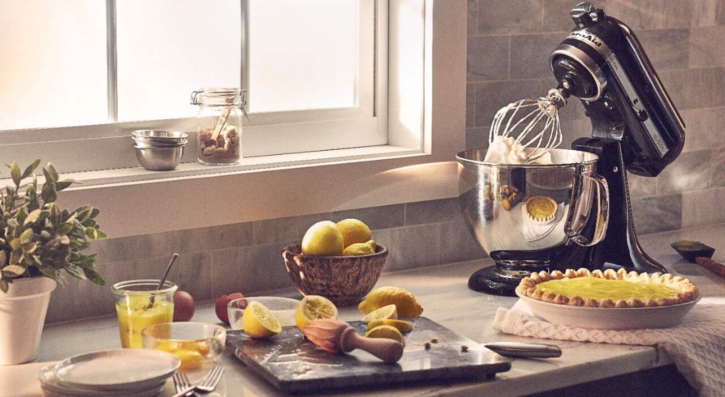 A black KitchenAid® stand mixer next to a lemon pie and lemon slices.