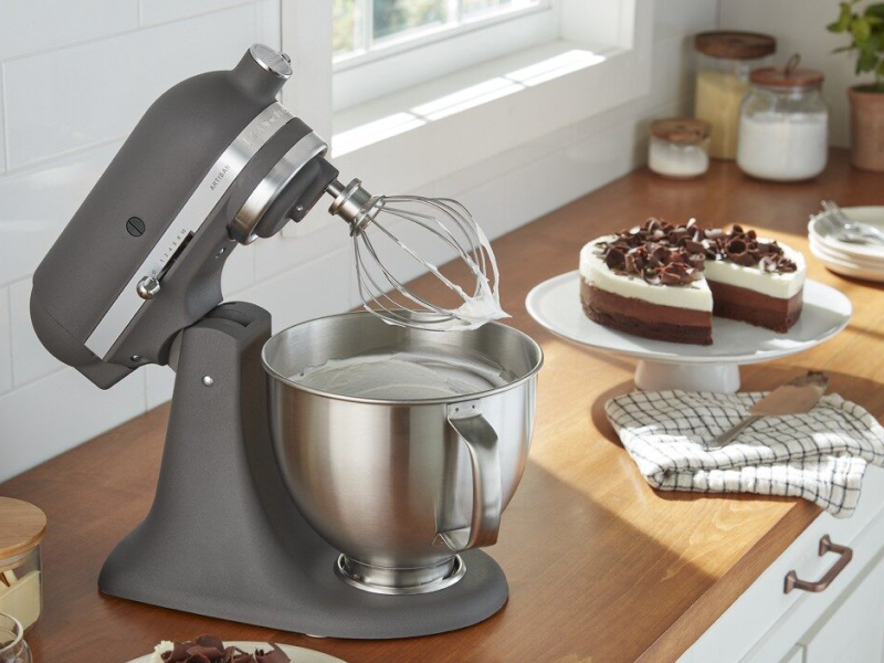 A black KitchenAid® stand mixer next to a cake on a counter.
