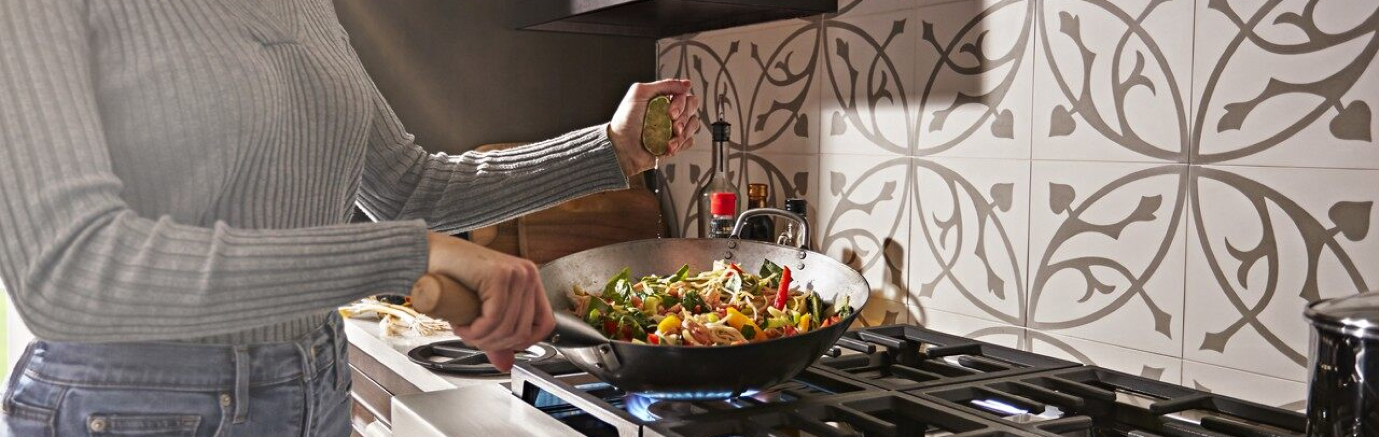 Person squeezing lime juice into a wok simmering vegetables