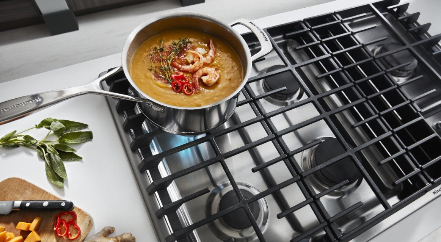 Saucepan with soup and garnishes on a gas stovetop