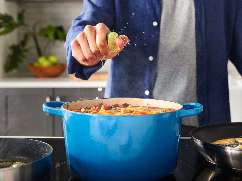 A person squeezing a lime over a rich stew cooking in a blue Dutch oven A person squeezing a lime over a rich stew cooking in a blue Dutch oven