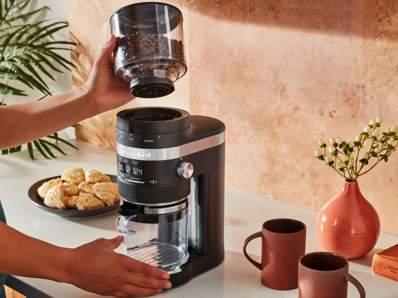 A woman using a black KitchenAid® coffee grinder to grind coffee beans A woman using a black KitchenAid® coffee grinder to grind coffee beans