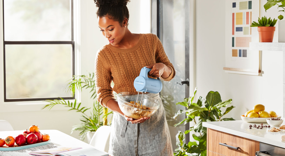 A woman reading a cookbook and holding a cordless hand mixer and a bowl A woman reading a cookbook and holding a cordless hand mixer and a bowl