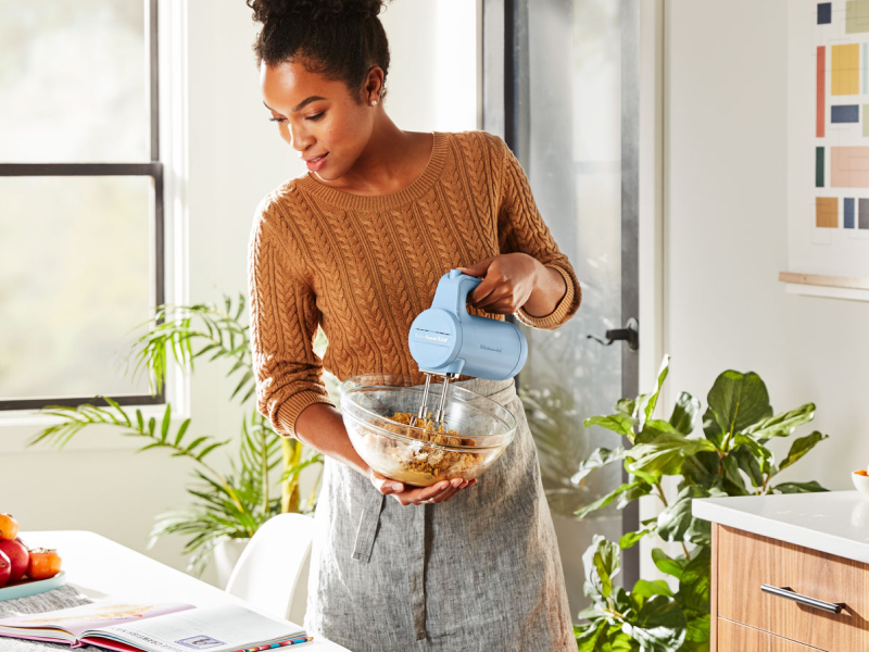 A woman reading a cookbook and holding a cordless hand mixer and a bowl A woman reading a cookbook and holding a cordless hand mixer and a bowl