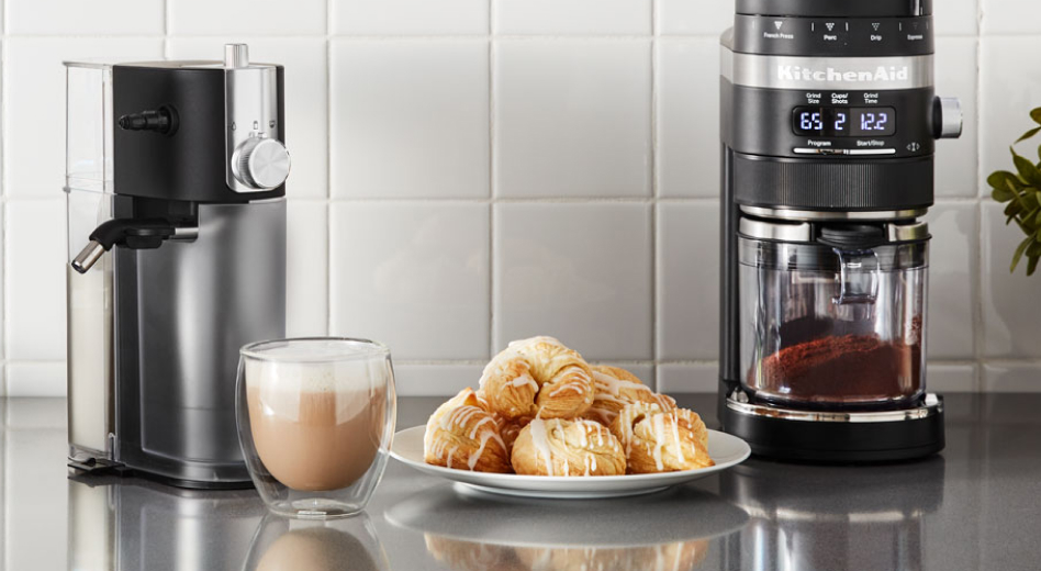 A cup of whipped coffee on a stainless steel countertop with baked goods and appliances A cup of whipped coffee on a stainless steel countertop with baked goods and appliances