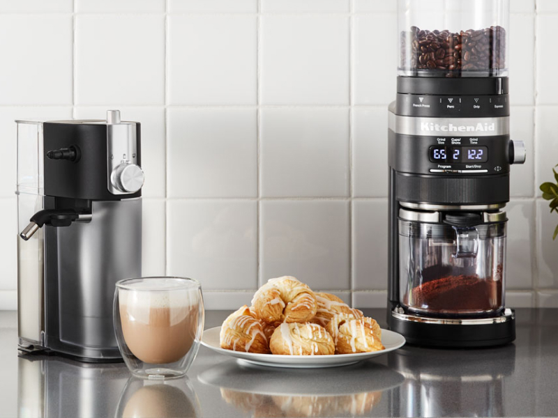 A cup of whipped coffee on a stainless steel countertop with baked goods and appliances A cup of whipped coffee on a stainless steel countertop with baked goods and appliances