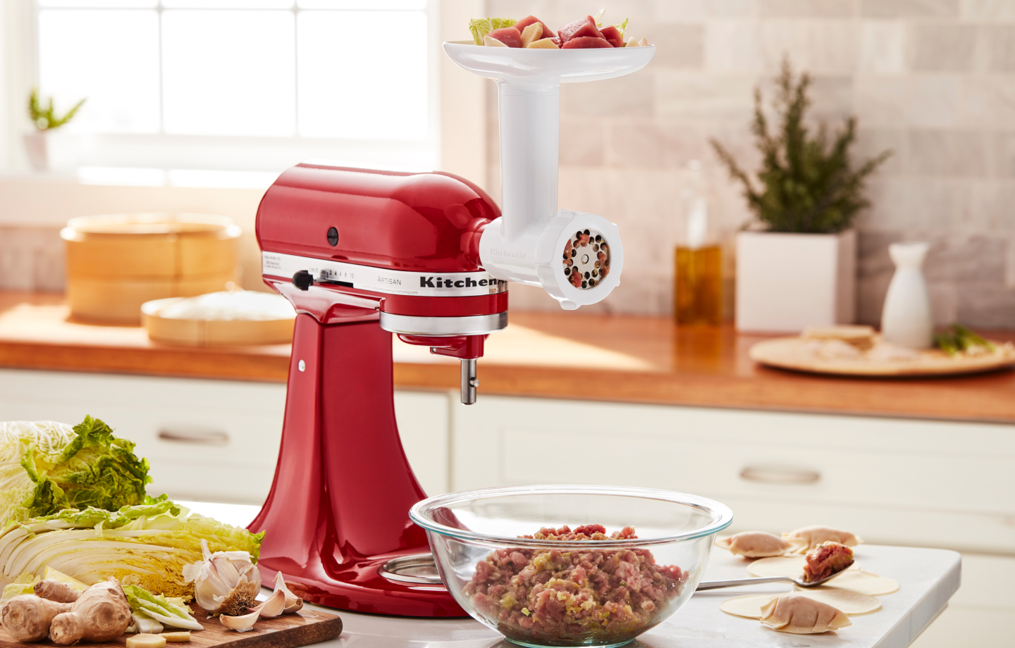 A red KitchenAid®  Stand Mixer with Food Grinder Attachment on the counter of a modern kitchen