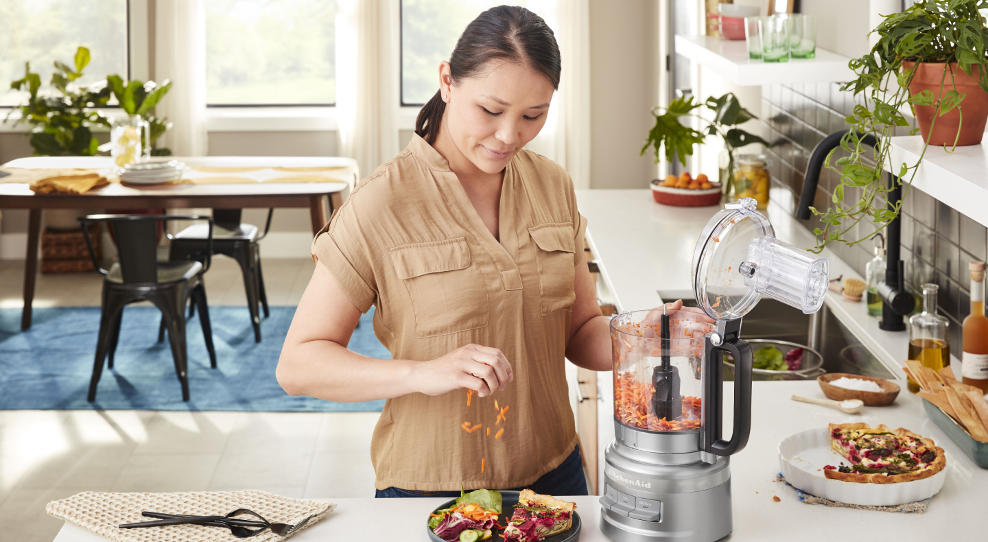 Woman placing carrots grated in KitchenAid® food processor on salad Woman placing carrots grated in KitchenAid® food processor on salad