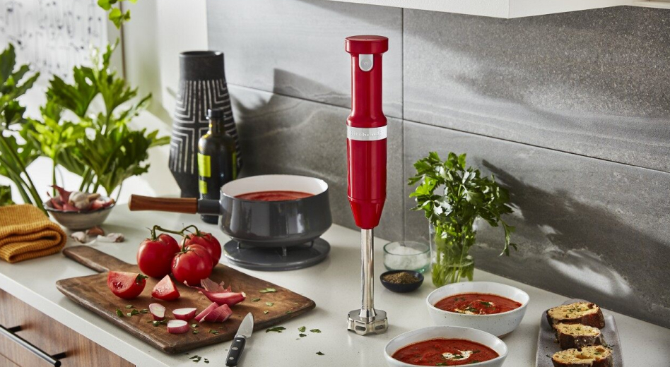 Red KitchenAid® Cordless Variable Speed Hand Blender with bowls of tomato soup Red KitchenAid® Cordless Variable Speed Hand Blender with bowls of tomato soup