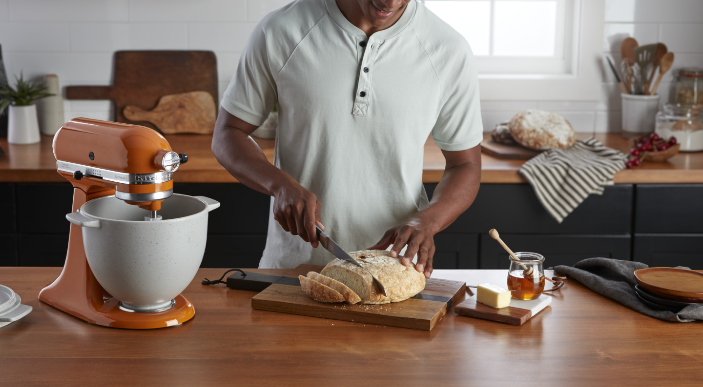 Person slicing bread next to an orange KitchenAid® stand mixer