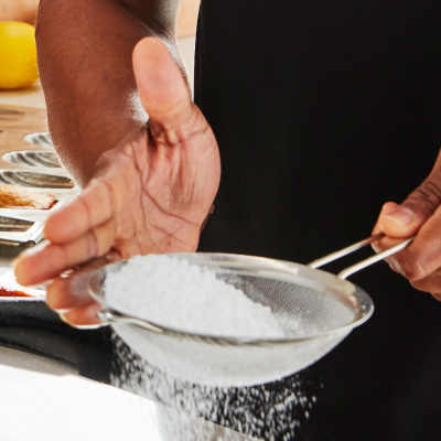 Person sifting sugar into a recipe